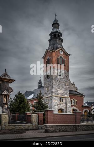Ancienne église en pierre et en brique avec tour d'horloge à Bialka Tatrzanska. Nuages sombres et sombres et ciel spectaculaire. Montagnes Tatra, Pologne Banque D'Images
