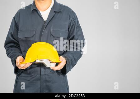 Cloes up Worker debout dans un coverall bleu tenant un casque de sécurité jaune isolé sur fond gris Banque D'Images