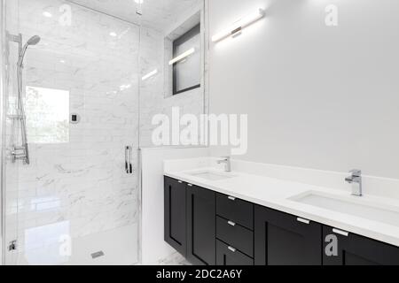 Salle de bains moderne avec meuble-lavabo noir, douche en marbre avec porte et murs en verre et quincaillerie chromée. Banque D'Images