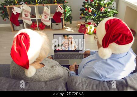 Grand-parents de couple senior en chapeaux de fête de Noël assis sur un canapé et discuter en ligne avec votre famille Banque D'Images