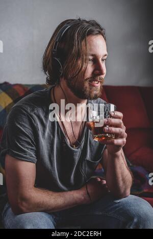 Homme barbu écoutant de la musique avec un casque et tenant le verre avec du thé dans la main Banque D'Images