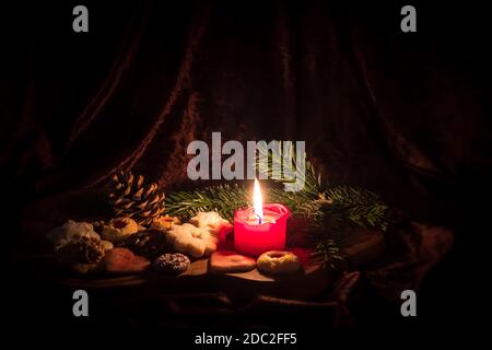 Bougie rouge allumée entre les biscuits de Noël décorés sur un panneau en bois devant un arrière-plan sombre Banque D'Images