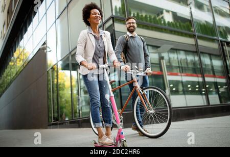 Deux personnes souriantes en voyage d'affaires avec scooter électrique, vélo allant au travail. Banque D'Images