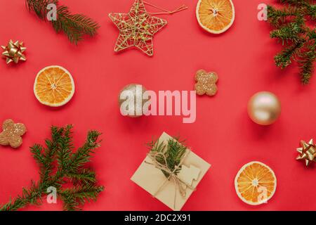 Appartement de Noël avec branches d'épicéa, cadeau, biscuits, oranges séchées et décorations de Noël sur fond rouge. Concept de la nouvelle année. Vue de dessus, plate Banque D'Images