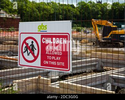 Panneau d'avertissement pour les enfants sur une clôture métallique protégeant un chantier avec un creuseur et des fondations en arrière-plan. Banque D'Images