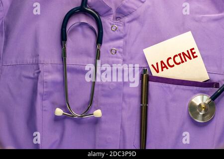 Uniforme médical, carte blanche avec les mots « vaccin », stylo métallique et stéthoscope. Concept médical et pandémique Covid-19. Banque D'Images