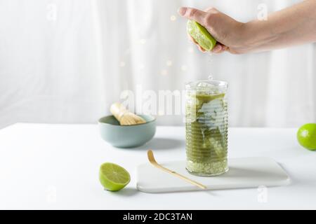 Femme à la main de la lime dans le verre avec du matcha latte vert glacé sur fond blanc. Limonade au matcha glacé. Banque D'Images