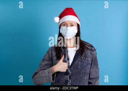 Gros plan d'une jeune femme asiatique portant un chapeau de père Noël et un masque médical de protection contre le virus, protection fiable Banque D'Images