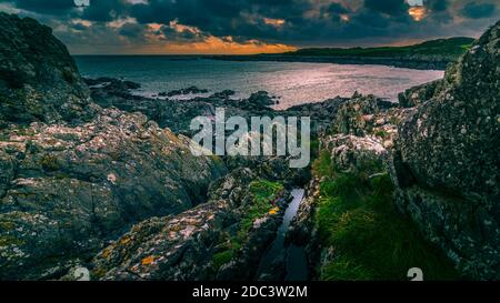Port de l'île de Whithorn situé dans un coucher de soleil spectaculaire, eau encore et soleil, plage rocheuse, falaises Banque D'Images