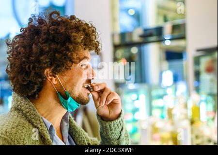 Jeune homme heureux barbu avec une peau saine et des cheveux bouclés agréable avec goût de chocolat bio fraîchement cuit, peut contenir un petit pièce d'une main Banque D'Images