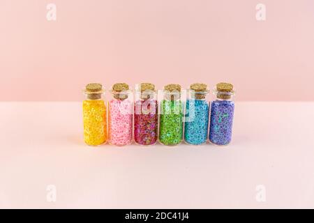 Petits flacons ou bocaux en verre avec bouchons scellés et étoiles brillantes multicolores sur fond rose. Décorations en sequins pour la créativité. Banque D'Images