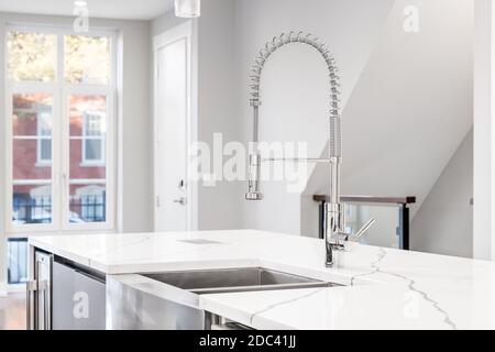 Un évier de cuisine avec un robinet en chrome, un évier à tablier en acier inoxydable et des plans de travail en granit blanc qui donnent sur un escalier. Banque D'Images