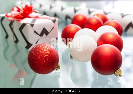 Des boules de Noël rouges et blanches sont dispersées sur la table en verre. Cadeau de Noël, papier d'emballage, noeud rouge. Gros plan. Noël du nouvel an. Le concept de Banque D'Images