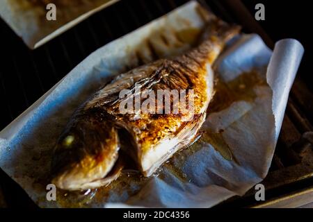 Barbecue au poisson Dorado sur papier parchemin.cuisson du bar de mer entier Faites griller en gros. Délicieux fruits de mer cuits pour le dîner Banque D'Images