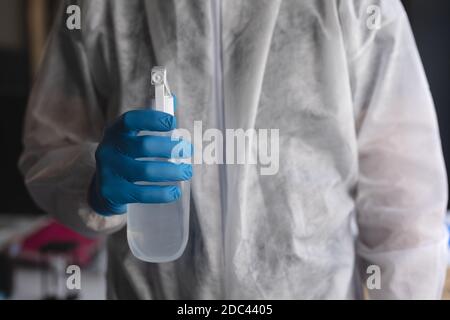 Section centrale de l'agent de santé dans des vêtements de protection contenant une bouteille de désinfectant au bureau moderne Banque D'Images
