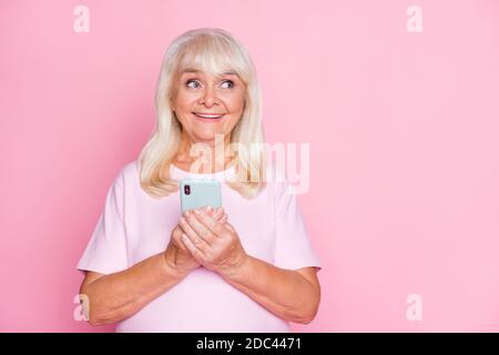 Photo portrait de la curieuse granny en gardant le smartphone en blanc espace souriant heureusement isolé sur fond rose pastel Banque D'Images