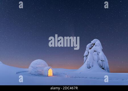 Igloo de neige lumineux de l'intérieur dans les montagnes d'hiver. Ciel étoilé avec comète en arrière-plan Banque D'Images