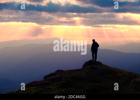 Seul touriste sur le bord de la falaise avec la toile de fond d'un paysage incroyable de montagnes au coucher du soleil Banque D'Images