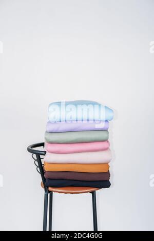 Pile de tissus aux couleurs pastel naturelles sur fond blanc. Tissus et vêtements disposés dans des piles soignées sur la chaise. Arrière-plan de la pile de tissus Banque D'Images