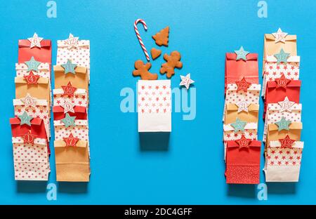 Fabrication de sacs-cadeaux de calendrier de l'Avent avec biscuits de pain d'épice et cannes de bonbons, sur fond bleu. Vue de dessus avec 24 sacs en papier pour l'arrivée de Noël. Banque D'Images