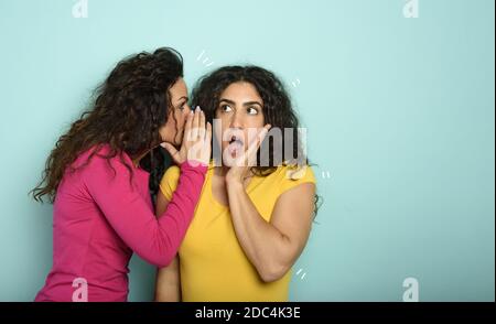 Femme parle dans l'oreille à un ami au sujet d'une grande promotion. Expression stupéfait. Fond cyan Banque D'Images