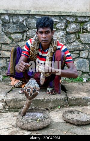 Un jeune charmeur de serpent avec un python enveloppé autour de son cou et un cobra dans un panier de canne se trouve sur le sentier de Pinnawala dans le centre du Sri Lanka. Banque D'Images