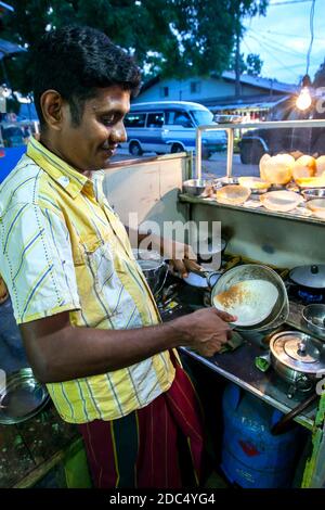 Un homme qui cuisine des trémies sur un poêle à gaz dans son restaurant près du temple de Kataragama au Sri Lanka. Les trémies sont une nourriture préférée au Sri Lanka. Banque D'Images