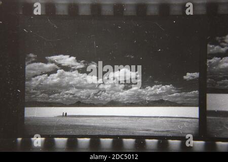 Belle photographie en noir et blanc vintage des années 1970 de deux personnes marchant le long de la plage d'été. Banque D'Images