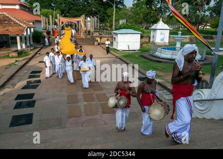 Un trompettiste et des tambours mènent une procession de pèlerins portant un tissu orange vers le Ruwanwelisiya Dagoba à Anuradhapura au Sri Lanka. Banque D'Images