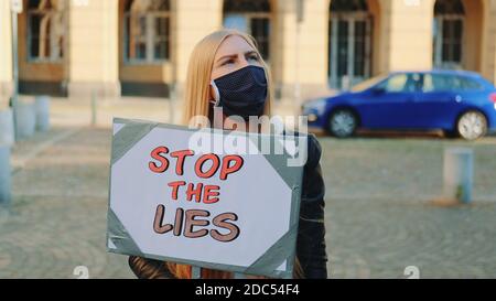 Femme inquiète dans un masque de protection avec une bannière de protestation appelant à arrêtez-vous en marchant dans la rue de la ville Banque D'Images