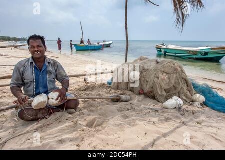 Un pêcheur heureux tend à ses filets à l'ombre d'un arbre sur la plage de la côte ouest de l'île Delft dans la région de Jaffna au Sri Lanka. Banque D'Images