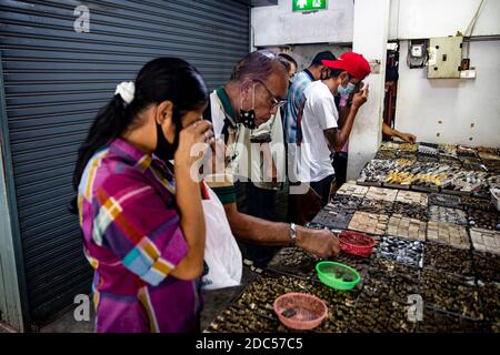 Les clients potentiels, certains utilisant la loupe, examinent de près les anciens amulettes bouddhistes dans un magasin de Tha Maharaj Pier Complex à Bangkok, en Thaïlande. Banque D'Images