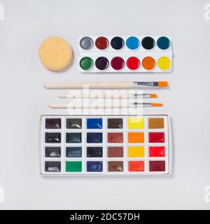 Kit artistique pour peindre avec de nouvelles peintures à l'aquarelle, des outils et des pinceaux sur fond blanc. Espace de travail artiste. Flat lay, vue de dessus Banque D'Images