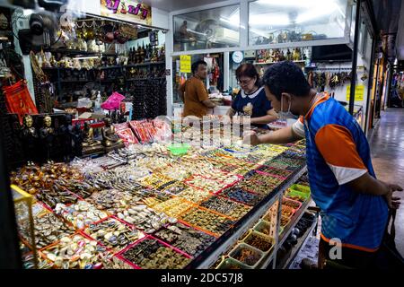 Les clients potentiels, certains utilisant la loupe, examinent de près les anciens amulettes bouddhistes dans un magasin de Tha Maharaj Pier Complex à Bangkok, en Thaïlande. Banque D'Images