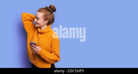 Une adorable femme aux cheveux rouges et aux taches de rousseur écoute musique sur un mur bleu de studio avec espace libre Banque D'Images