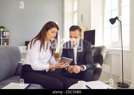 Une femme secrétaire avec une tablette numérique en mains présente des documents électroniques à son patron. Banque D'Images