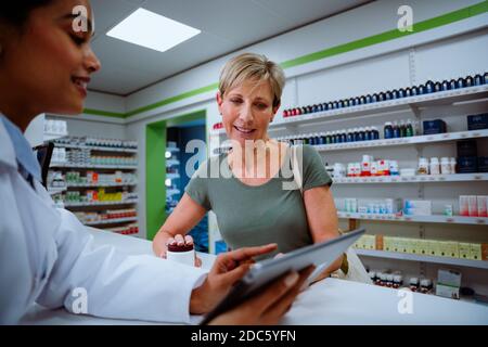 Une mère caucasienne discutant avec un jeune chimiste interne à la recherche du numérique comprimé en pharmacie Banque D'Images