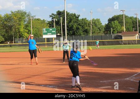 Les filles jouant au softball avec le ciel bleu et les arbres avec la saleté rouge sur le terrain de jeu dans le Kansas. Banque D'Images