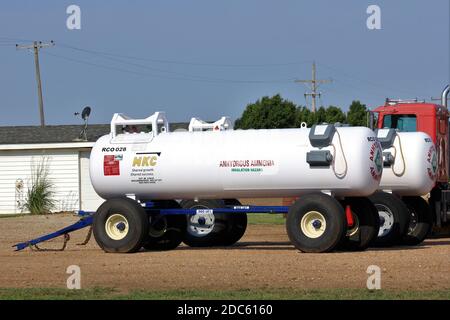 Réservoirs d'ammoniac anhydre dans une cour de ferme avec un camion et un bâtiment à ciel bleu au Kansas. Banque D'Images