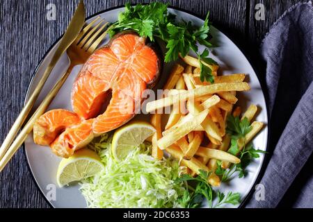 steaks de saumon servis avec des pommes de terre frites et du coleslaw sur une assiette sur une table en bois sombre, vue horizontale depuis le dessus, plat Banque D'Images