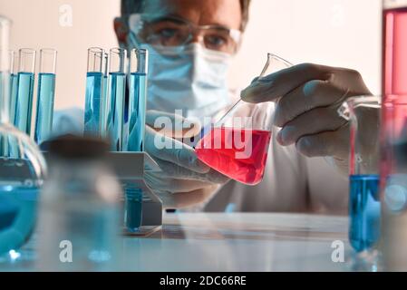 Détail d'un scientifique manipulant soigneusement un liquide rouge dans un flacon sur une table de laboratoire. Composition horizontale. Vue avant. Banque D'Images