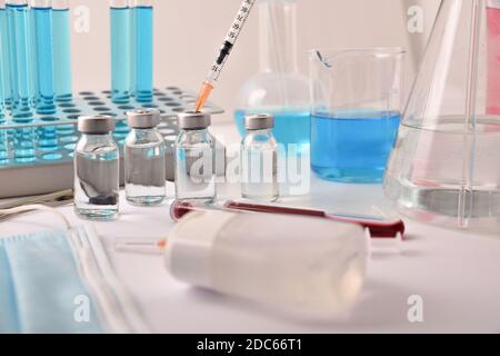 Vaccin en flacon avec seringue sur un banc de laboratoire avec éléments de protection et verrerie médicale et chimique. Composition horizontale. Vue avant. Banque D'Images