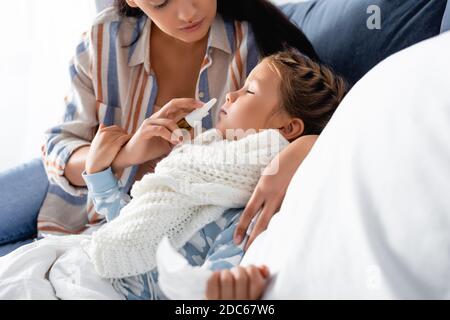 femme utilisant un spray nasal à une fille malade souffrant d'écoulement liquide nez sur un premier plan flou Banque D'Images