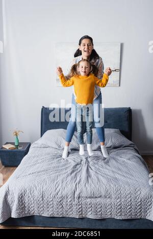 mère et fille gaies tenant les mains tout en sautant sur le lit Banque D'Images
