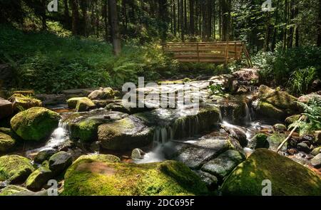 Ruisseau idyllique dans la forêt avec de grandes pierres de mousse et un pont en bois Banque D'Images