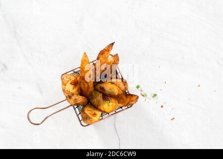 Pose à plat. Quartiers de pommes de terre fraîchement cuits avec épices dans un panier en fil métallique. Banque D'Images