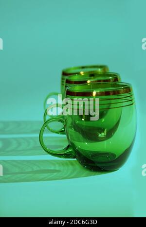 trois tasses en verre vert avec poignées se tiennent de suite sur fond bleu, format vertical Banque D'Images