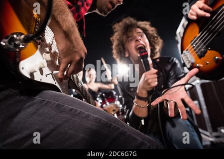 KIEV, UKRAINE - 25 AOÛT 2020 : vue à angle bas des chants dans le microphone près des guitaristes avec rétroéclairage sur fond flou Banque D'Images