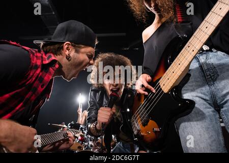 KIEV, UKRAINE - 25 AOÛT 2020 : vue en contre-angle d'un chanteur maussal regardant un appareil photo tout en criant avec un guitariste rétroéclairé sur fond flou Banque D'Images