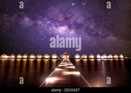 Paysage de nuit incroyable, lumières LED avec jetée et villas sur l'eau. Vue sur le ciel de la voie lactée, vacances d'été parfaites, scène de vacances. Complexe tropical Banque D'Images
